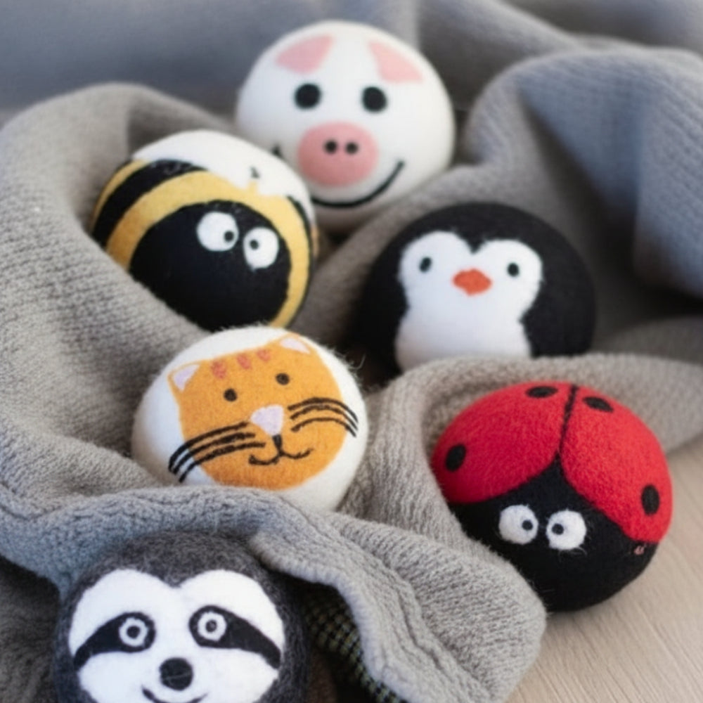 Colorful felt critter eco dryer balls in bee, pig, cat, sloth designs on red blanket