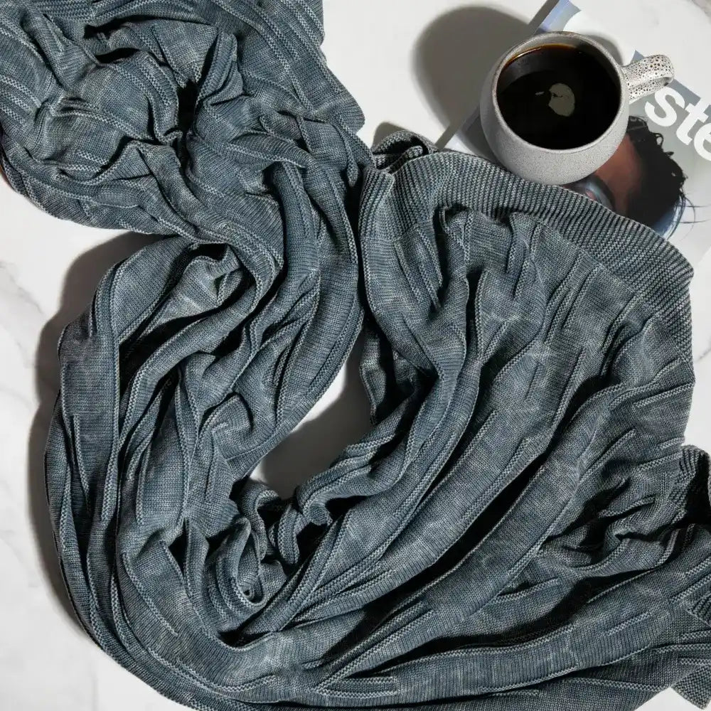 A throw blanket featuring a smooth, monochromatic textural knit in denim blue colors.