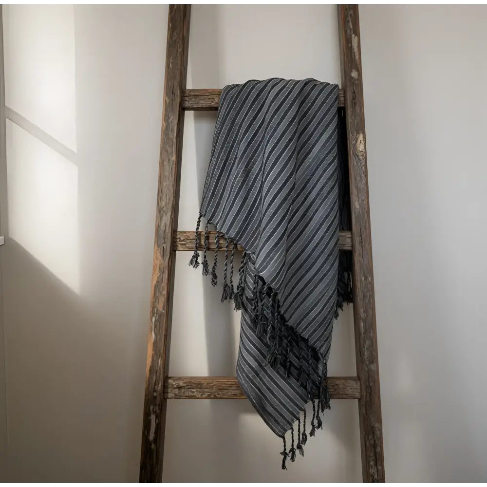 A handmade turkish towel with dark stripes in gray and white woven cotton draped over a rustic wooden ladder