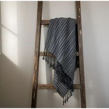 A handmade turkish towel with dark stripes in gray and white woven cotton draped over a rustic wooden ladder