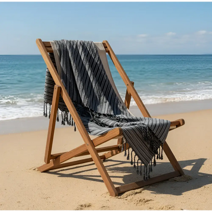 A handmade dark stripes towel in gray and white draped over a wooden folding chair perfect for beach use