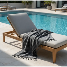 Gray striped dark stripes towel with tassels handmade turkish towels draped on wooden lounge chair by the pool