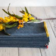 Stack of dark denim chambray cloth napkins with colorful stitched edges for stylish dining