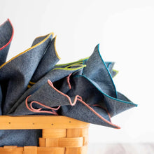 Basket of folded denim chambray cloth napkins with colorful stitched edges for stylish dining
