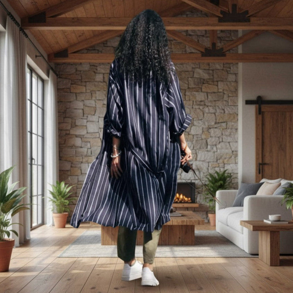 Person in a striped robe walking through a modern living room with wooden floors and stone walls.