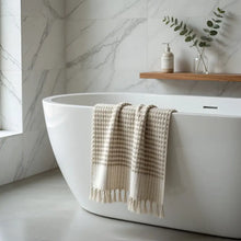 Beige dotted turkish terry hand loomed bath towel with tassels draped over white bathtub in taupe color