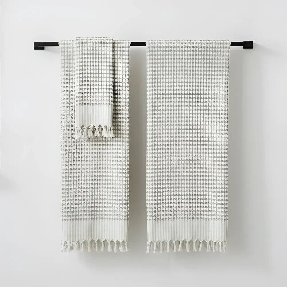 Two beige and gray checkered hand loomed bath towels with fringed edges hanging on black bar in taupe turkish terry bath