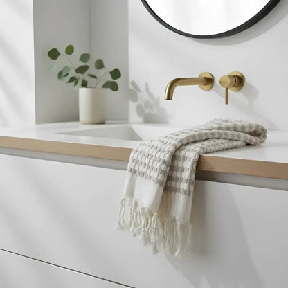 A soft off-white dotted turkish terry hand loomed bath towel with gray checks and fringed edges on a bathroom countertop