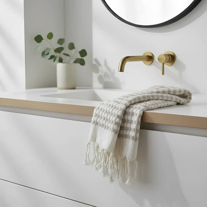 A soft off-white dotted turkish terry hand loomed bath towel with gray checks and fringed edges on a bathroom countertop
