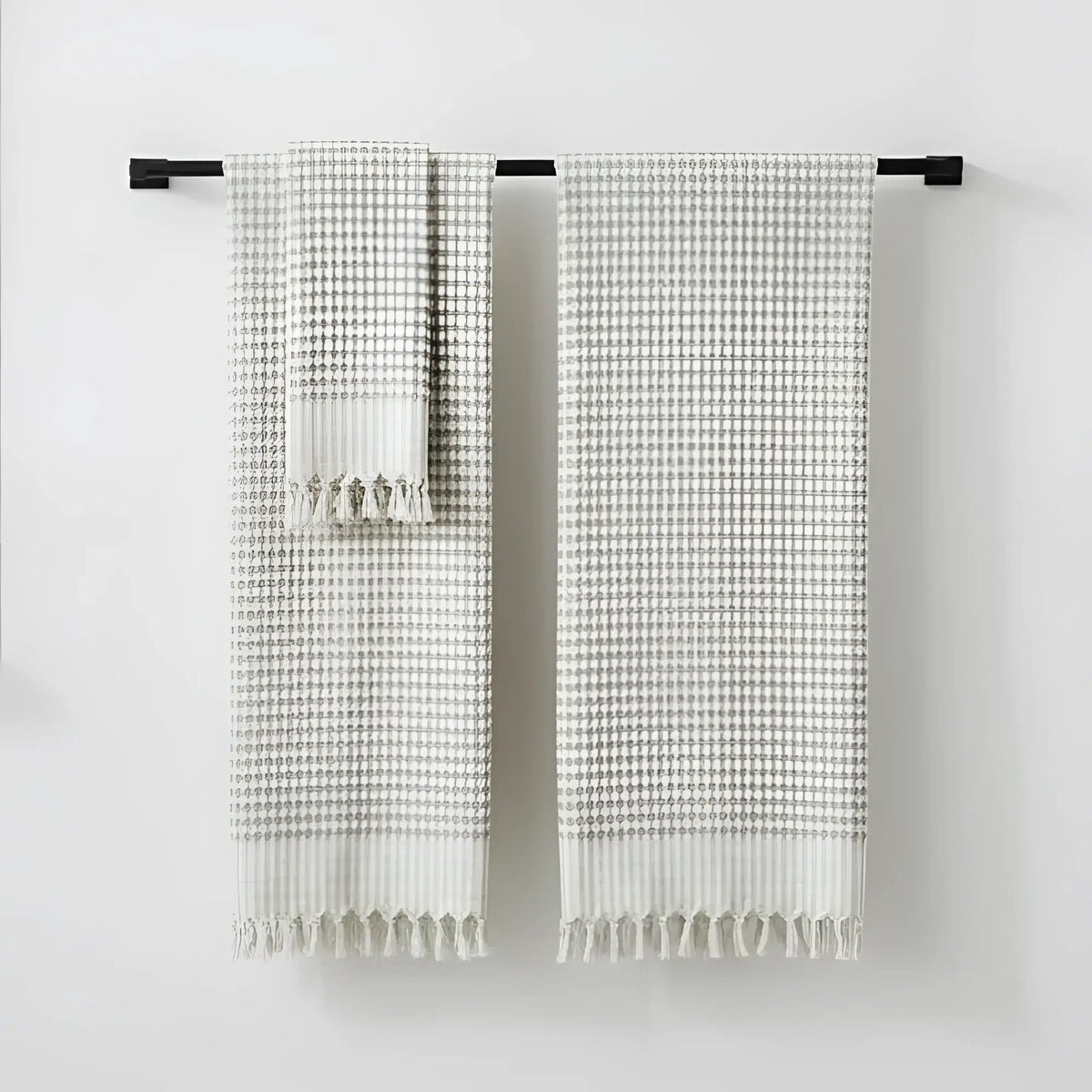 Two beige and gray checkered hand loomed bath towels with fringed edges hanging on black bar in taupe turkish terry bath