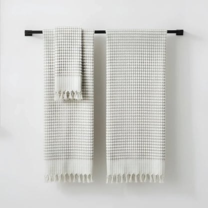 Two beige and gray checkered hand loomed bath towels with fringed edges hanging on black bar in taupe turkish terry bath