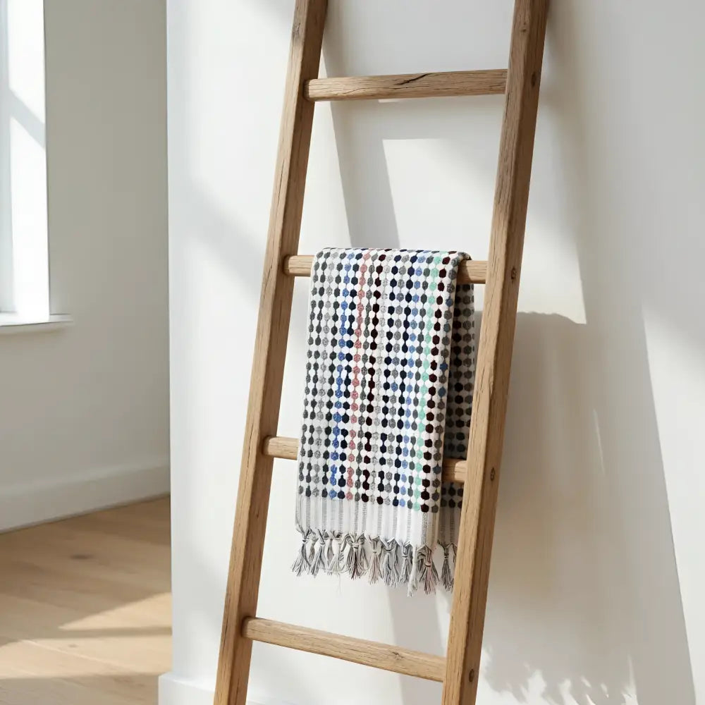 A colorful flamingo dotted turkish cotton terry oversized hand towel with fringed edges hanging on a wooden ladder