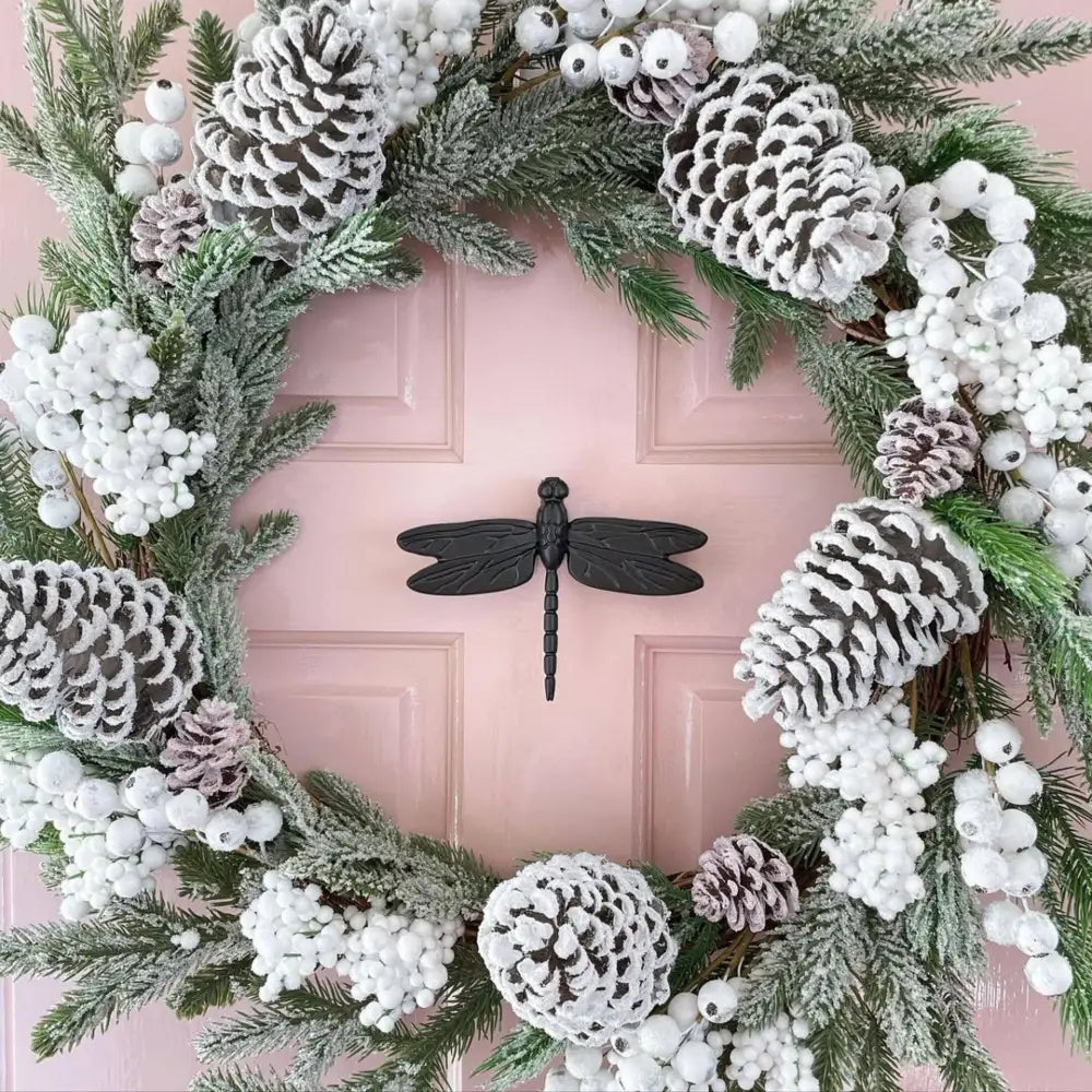 Decorative wreath with pinecones, berries, and a dragonfly door knocker on a pink door.