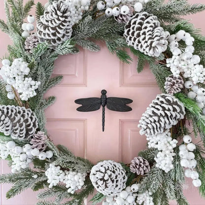 Decorative wreath with pinecones, berries, and a dragonfly door knocker on a pink door.