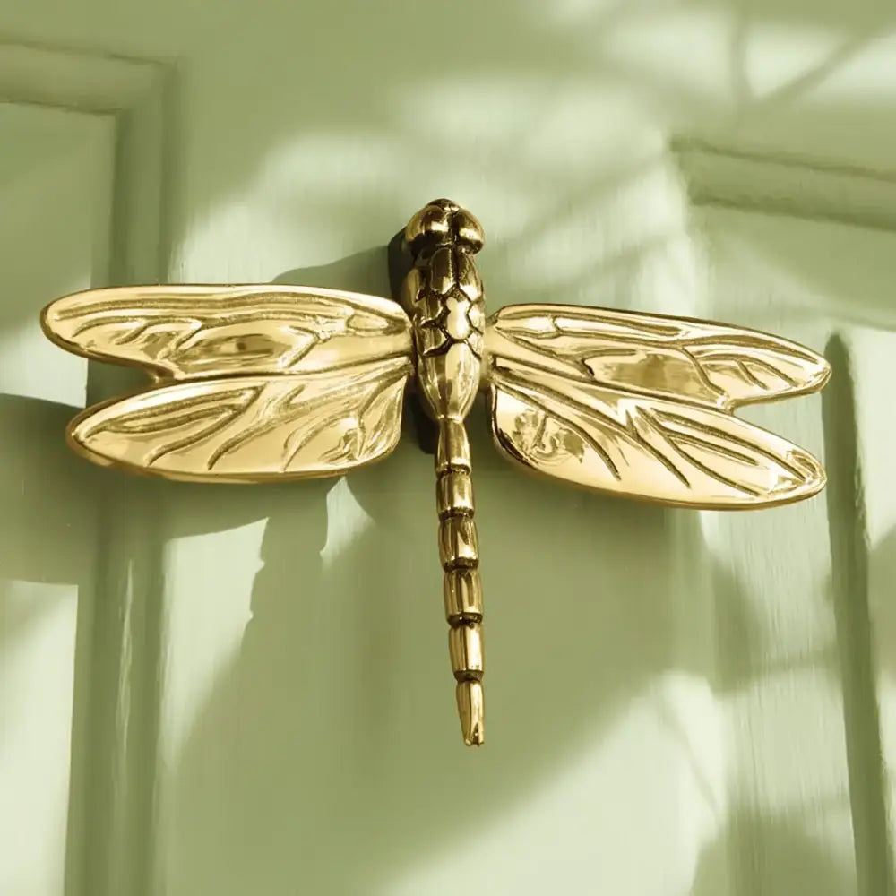 Gold dragonfly-shaped door knocker on a wooden door