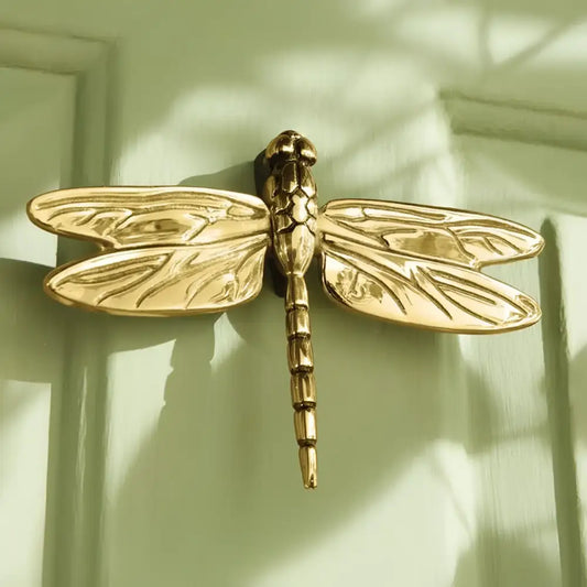 Gold dragonfly-shaped door knocker on a wooden door
