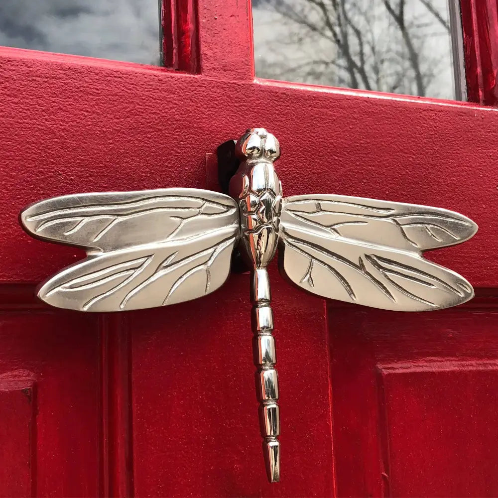 Silver dragonfly-shaped door knocker on a red door