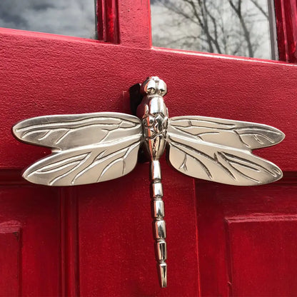 Silver dragonfly-shaped door knocker on a red door