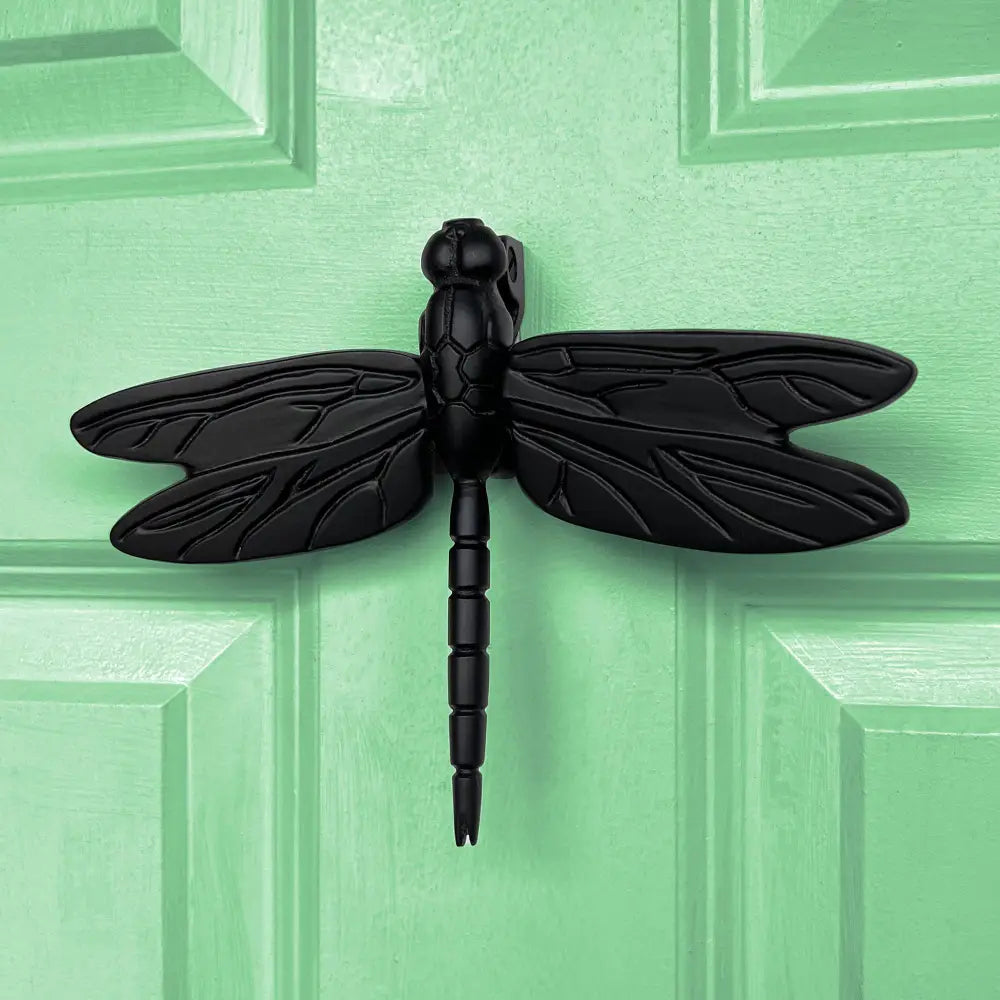 Black dragonfly-shaped door knocker on a green wooden door
