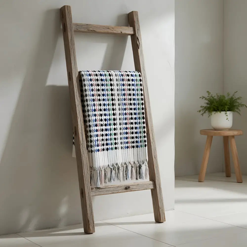 A rustic wooden ladder with a flamingo dotted turkish bath towel featuring multicolored checks and tasseled fringe