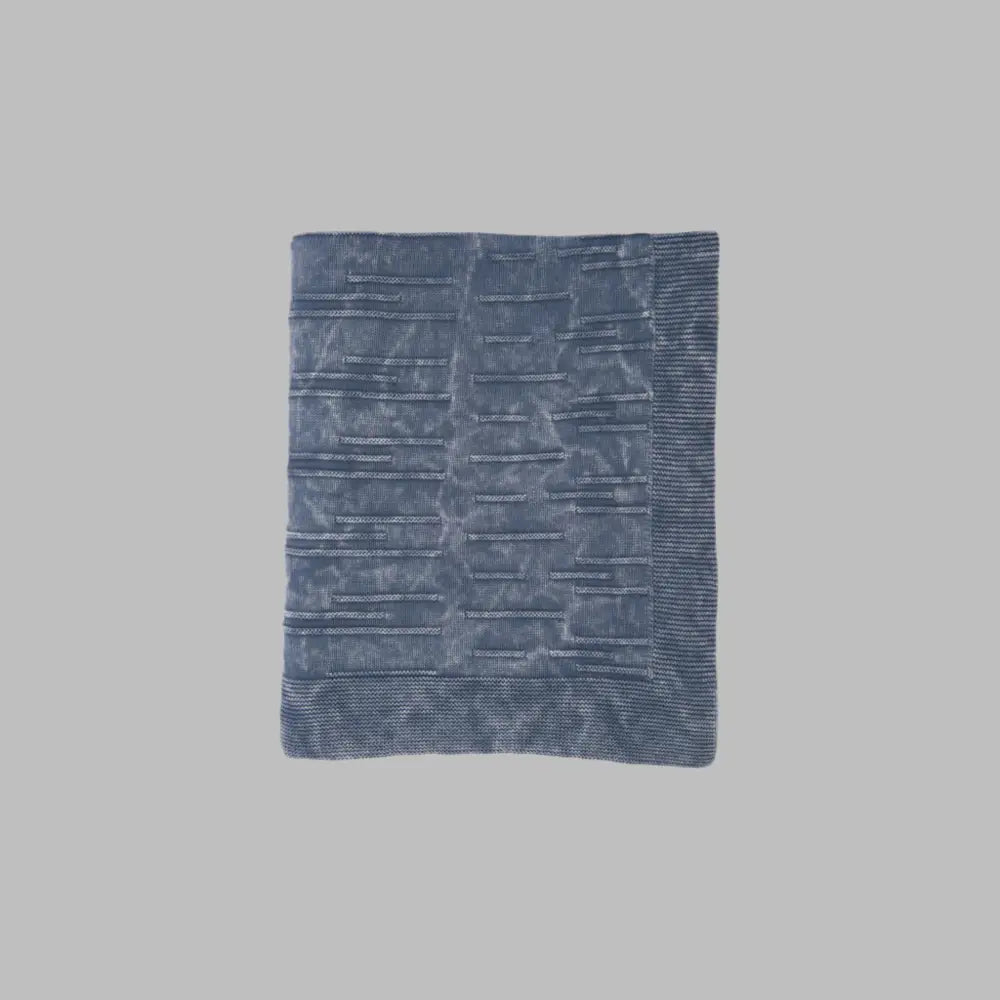 A throw blanket featuring a smooth, monochromatic textural knit in denim blue colors.