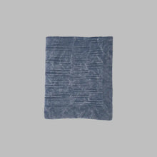 A throw blanket featuring a smooth, monochromatic textural knit in denim blue colors.