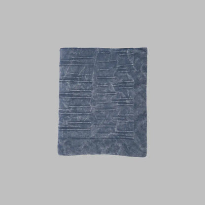 A throw blanket featuring a smooth, monochromatic textural knit in denim blue colors.