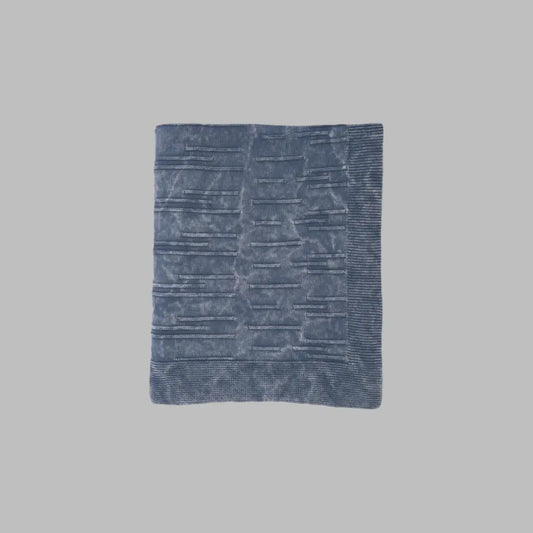 A throw blanket featuring a smooth, monochromatic textural knit in denim blue colors.