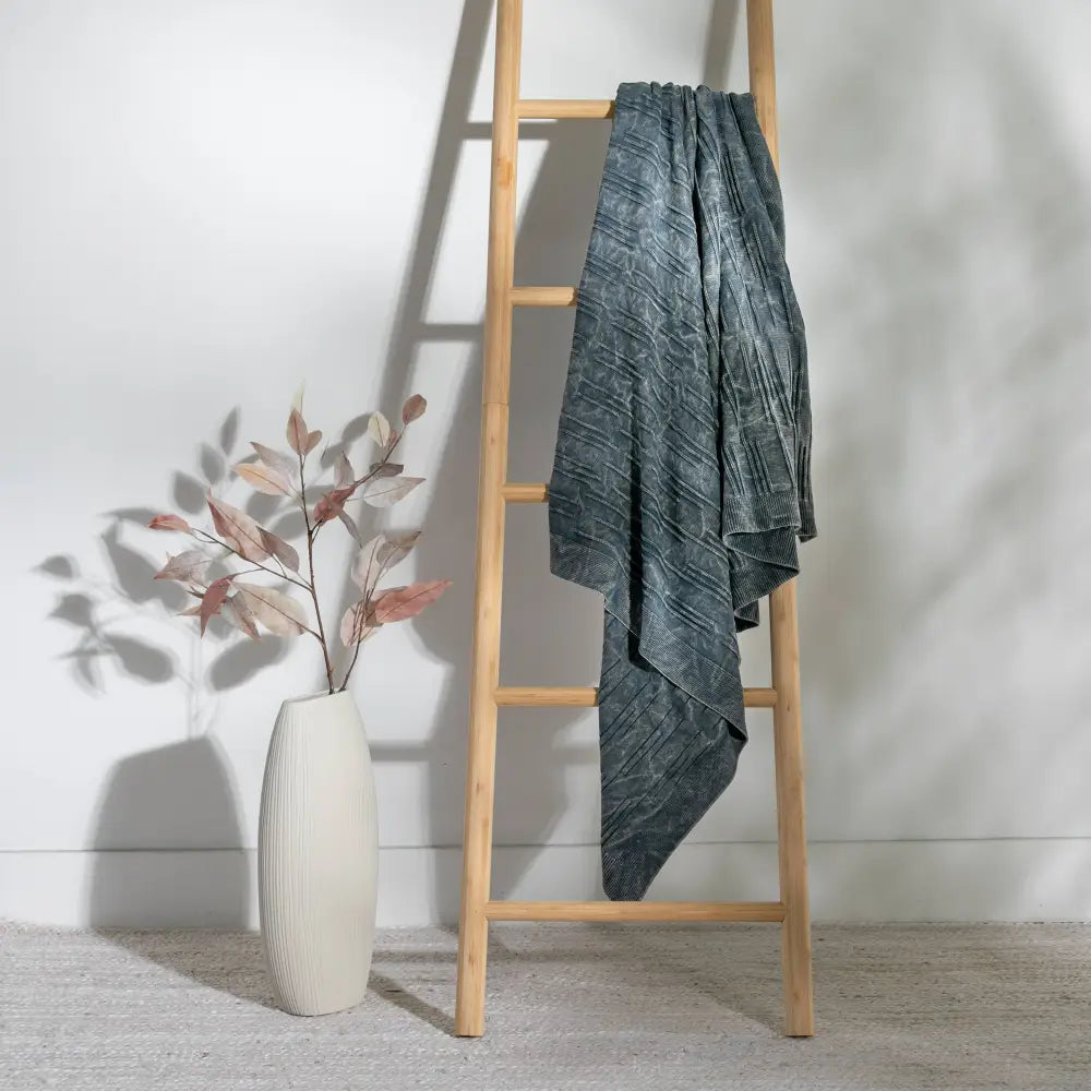 A throw blanket featuring a smooth, monochromatic textural knit in denim blue colors.