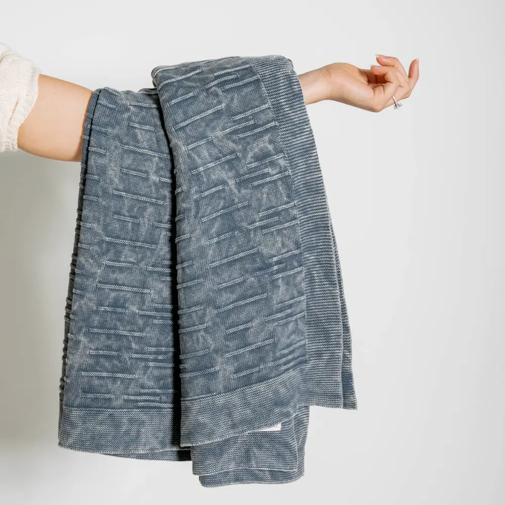 A throw blanket featuring a smooth, monochromatic textural knit in denim blue colors.