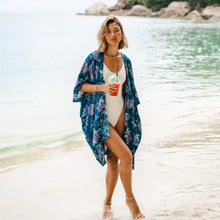 Woman in a white swimsuit and teal floral kimono cover enjoying a drink