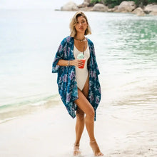 Woman in a white swimsuit and teal floral kimono cover enjoying a drink