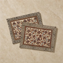 Beige cotton vines placemats set with intricate brown and black floral embroidery and decorative geometric border