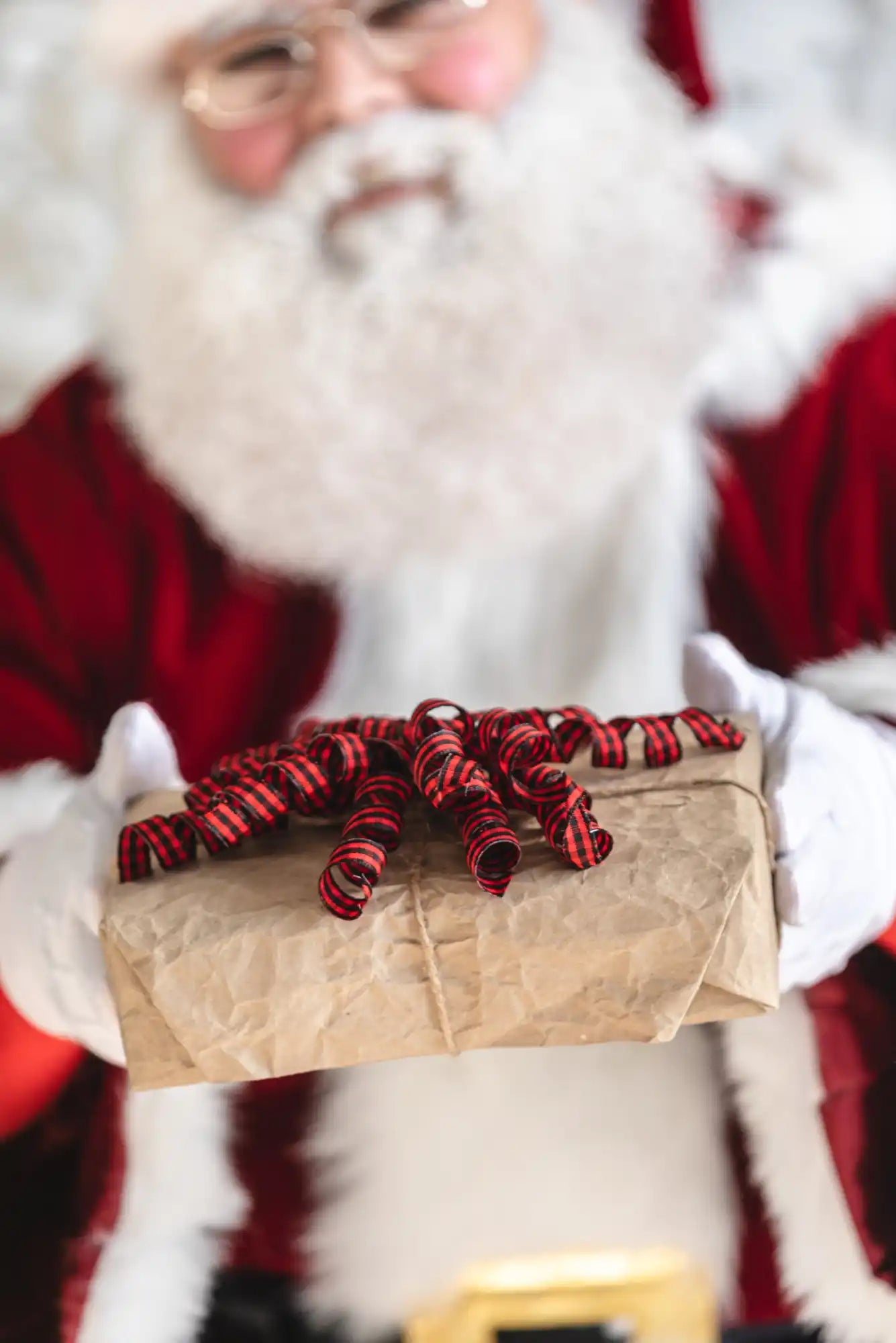 A gift wrapped in brown paper with red and black striped curly ribbon.