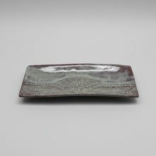 Decorative green rectangular plate with intricate patterns on a light-colored wall.