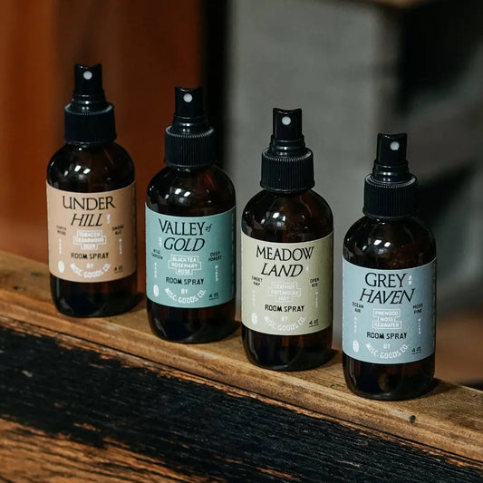 Four room spray bottles on a rustic wood shelf