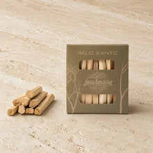 A box of Palo Santo incense sticks by Luna Sundara sits on a light beige stone surface, with several loose incense sticks placed beside the box.
