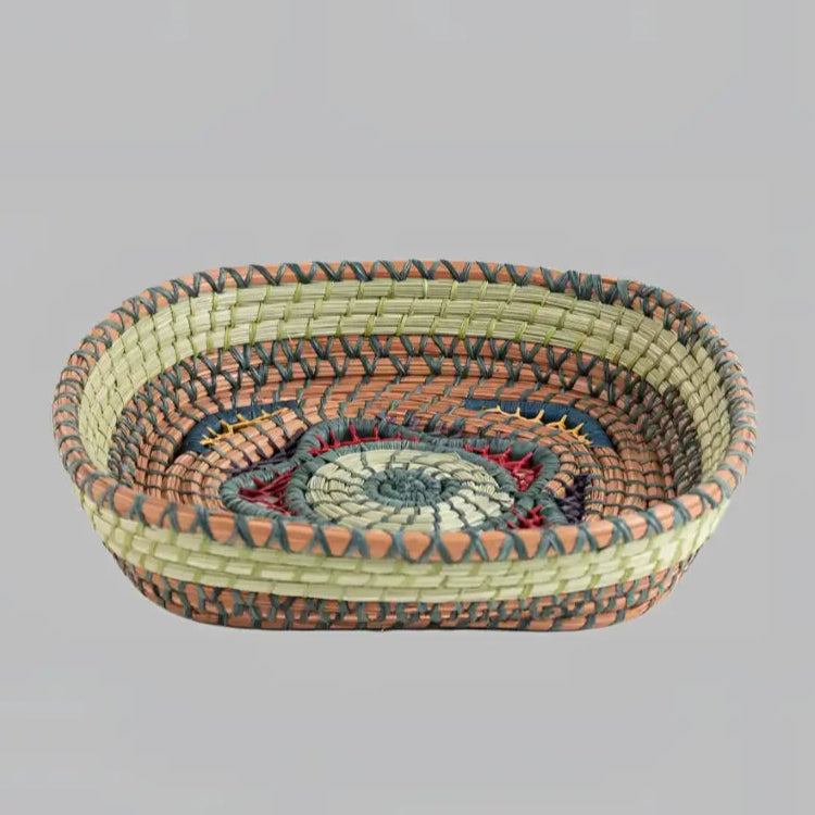 Intricately woven basket of native wild grass, and pine needles with colorful raffia accents.