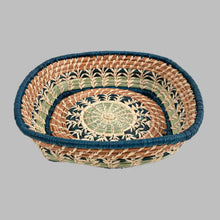 A basket featuring a variety of delicate raffia stitches on coils of pine needles and pajón, a native grass that grows in the highlands of Guatemala. Indigo blue raffia and pine needles accent the lovely design
