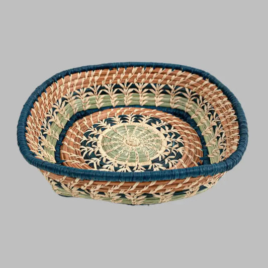 A basket featuring a variety of delicate raffia stitches on coils of pine needles and pajón, a native grass that grows in the highlands of Guatemala. Indigo blue raffia and pine needles accent the lovely design