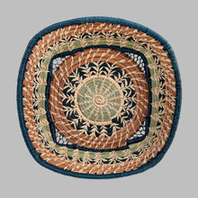 A basket featuring a variety of delicate raffia stitches on coils of pine needles and pajón, a native grass that grows in the highlands of Guatemala. A central circle transitions to a square basket. Indigo blue raffia and pine needles accent the lovely design
