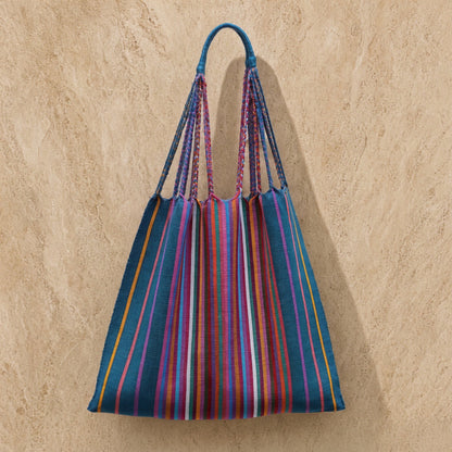 A vibrant hammock tote bag handwoven by mayan artisans in mexico with teal pink orange stripes and braided handles wearable art