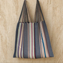 A stylish hammock tote bag handwoven by mayan artisans in mexico with navy beige and brown striped design and braided handles
