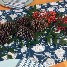 A hand block printed teal floral table runner featuring brown pinecones and red berries with azo free dyes