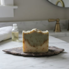 A handmade soapstone leaf soap dish with a rectangular cream wrapped soap tied with a brown ribbon