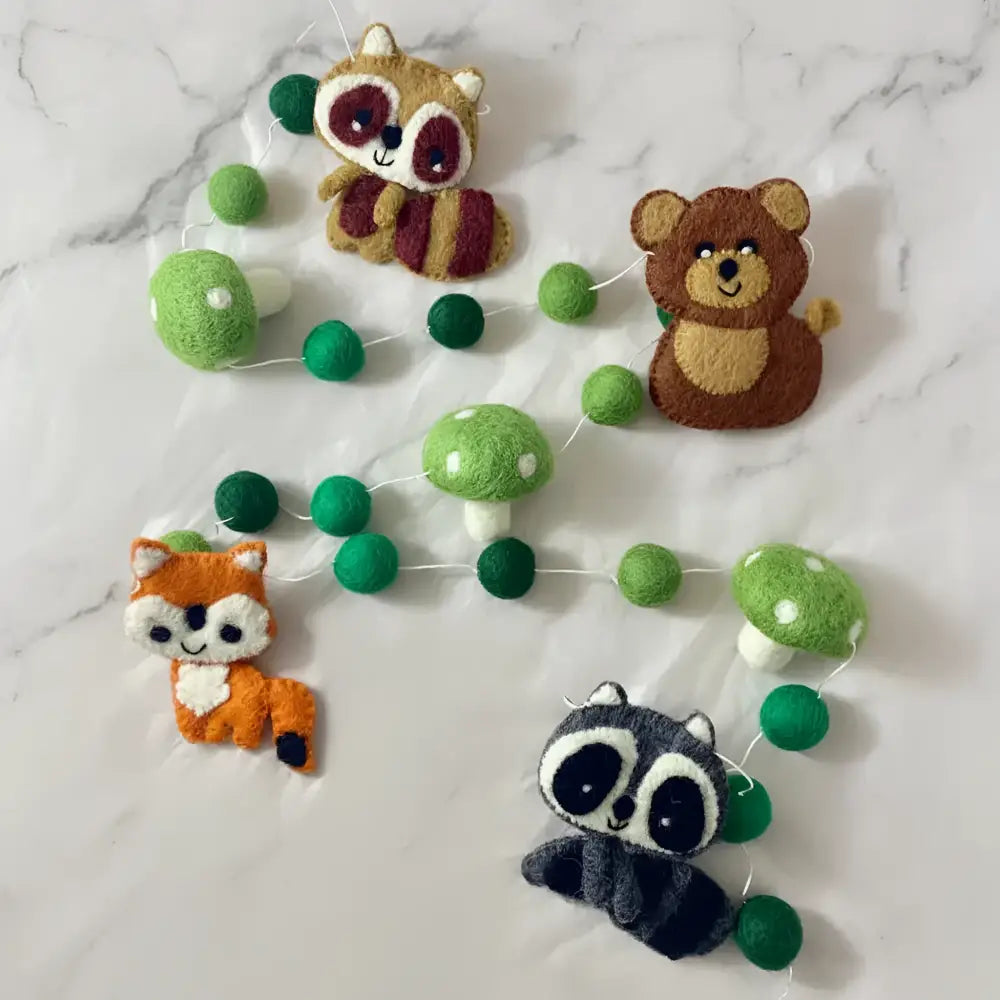A whimsical forest friends hand-felted wool garland with embroidered raccoons bears foxes and mushrooms in soft earthy tones