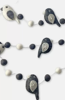 A charming black and white felted wool bird garland with embroidered details hanging on a porch 