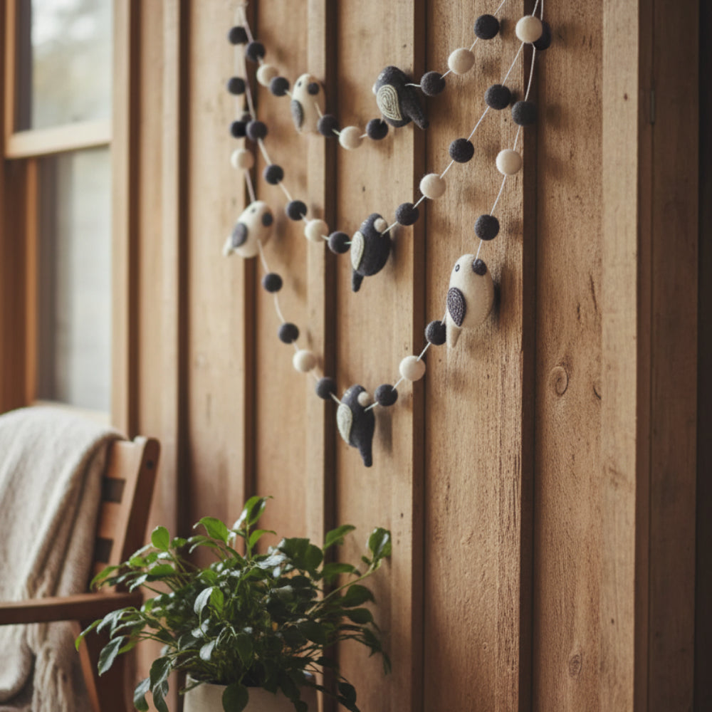 A charming black and white felted wool bird garland with embroidered details hanging on a porch 