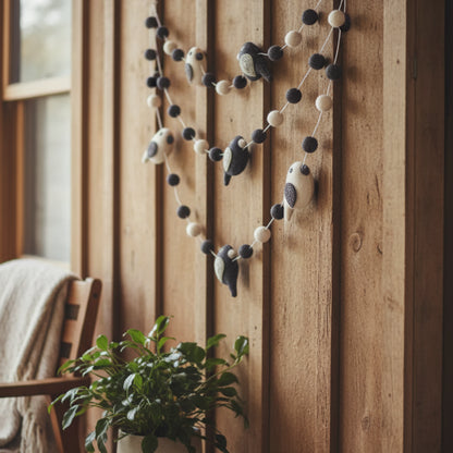 A charming black and white felted wool bird garland with embroidered details hanging on a porch 