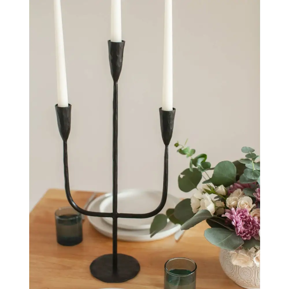 Black three-arm hand-forged iron candelabra with white taper candles for premium decor